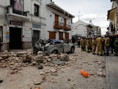 Petugas penyelamat berdiri di samping mobil yang hancur oleh puing-puing setelah gempa bumi di Cuenca, Ekuador, Sabtu (18/3/2023). (AP Photo/Xavier Caivinagua)