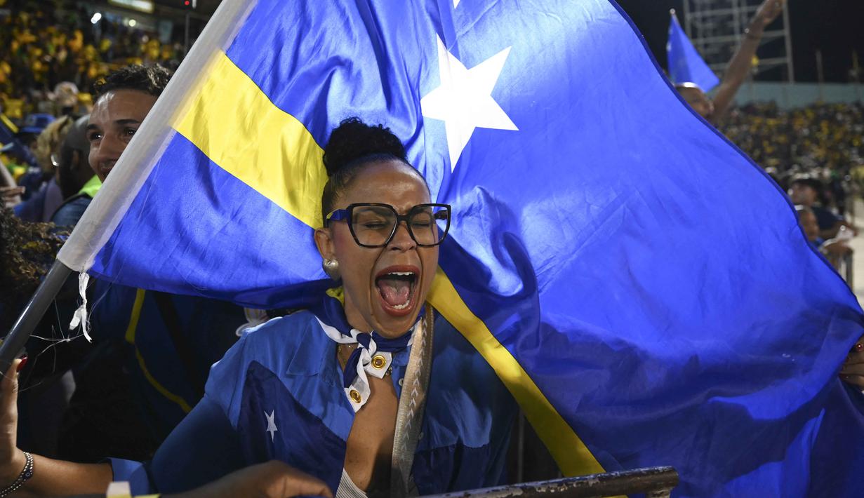 Timnas Curacao hanya terpaut satu poin dari Jamaika yang berada di peringkat kedua. Tampak dalam foto, suporter Timnas Curacao merayakan hasil imbang melawan Jamaika pada Grup B Kualifikasi Piala Dunia 2026 zona CONCACAF di Independence Park Stadium, Jamaika pada 18 November 2025. (Ricardo MAKYN/AFP)