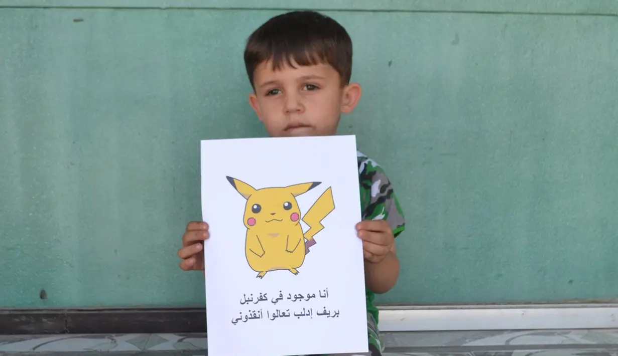 Seorang bocah Suriah memegang kertas bergambar karakter Pokemon bertuliskan "Aku di Kafr NABL di pedesaan Idlib, datang dan selamatkan aku", Suriah (22/7). (REUTERS)