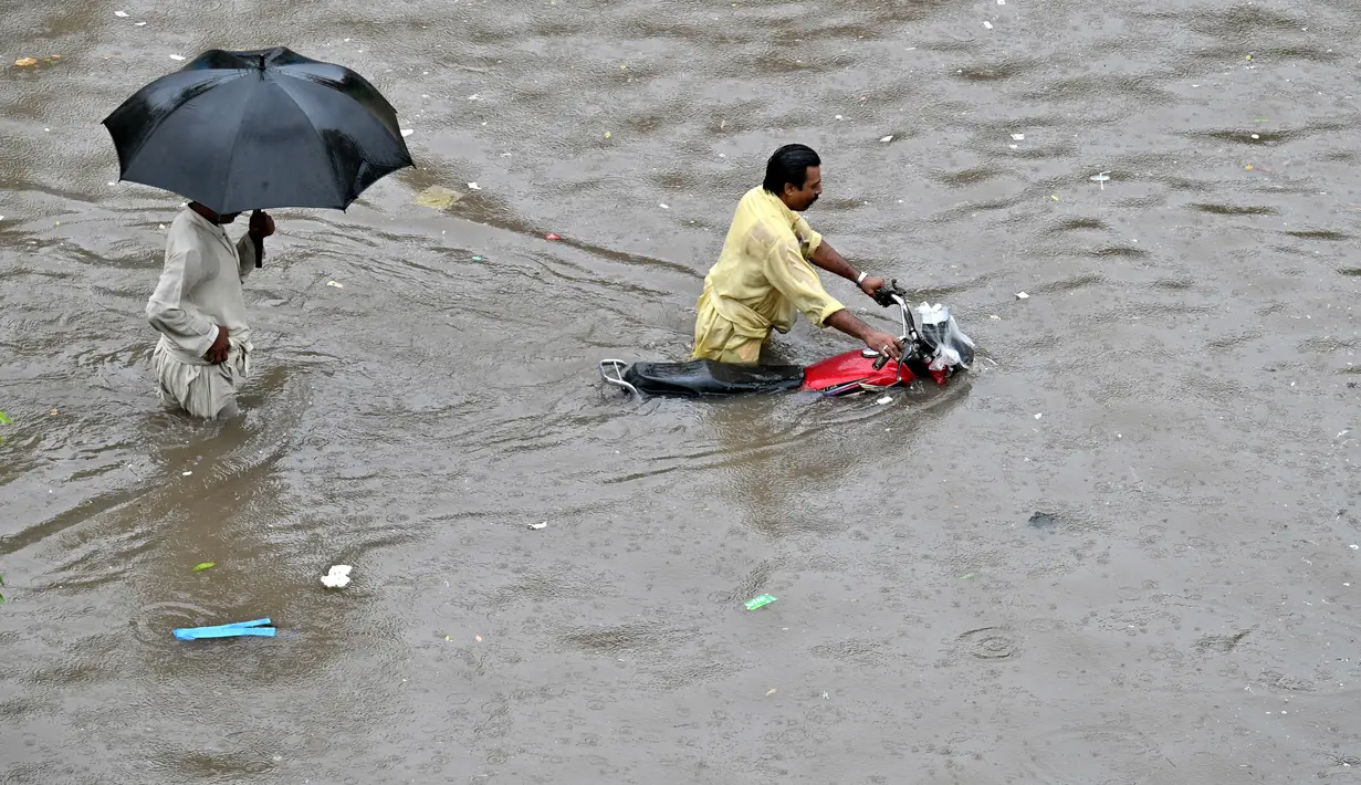 Seorang pengendara sepeda motor mendorong sepedanya melalui jalan yang banjir setelah hujan lebat di Lahore pada 5 Juli 2023. (AFP/Arif Ali)