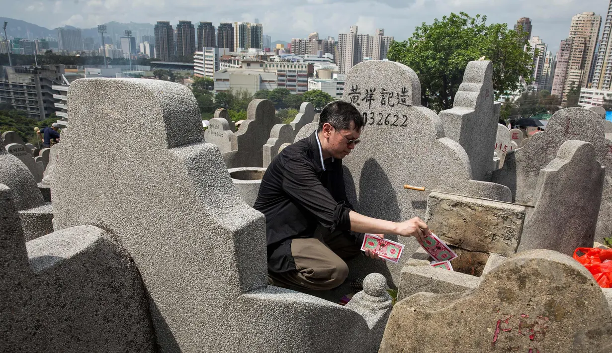 Seorang pria membakar uang kertas di makam seorang kerabat selama festival Qingming di pemakaman di Hong Kong (5/4). Biasanya warga cenderung membuat persembahan untuk keluarga atau kerabat mereka agar tetap nyaman di akhirat. (AFP Photo/Isaac Lawrence)