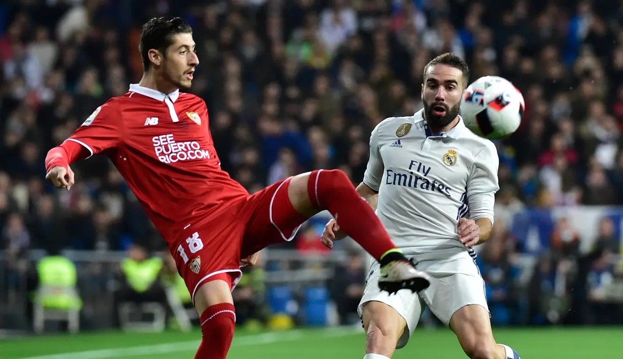 Bek Sevilla, Sergio Escudero (kiri) berusaha membuang bola dari kejaran bek Real Madrid, Dani Carvajal pada pertandingan pertama babak 16 besar Copa del Rey di Santiago Bernabeu, Spanyol (5/1). Madrid menang atas Sevilla 3-0. (AFP Photo/Gerard Julien)