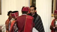 Presiden Joko Widodo (Jokowi) bereaksi setelah diberikan kain ulos oleh Pemangku Hutan Adat dari Tombak Haminjon (Kemenyan) Provinsi Sumatera Utara usai pencanangan pengakuan Hutan Adat di Istana Negara Jakarta, Jumat (30/12). (Liputan6.com/Faizal Fanani)