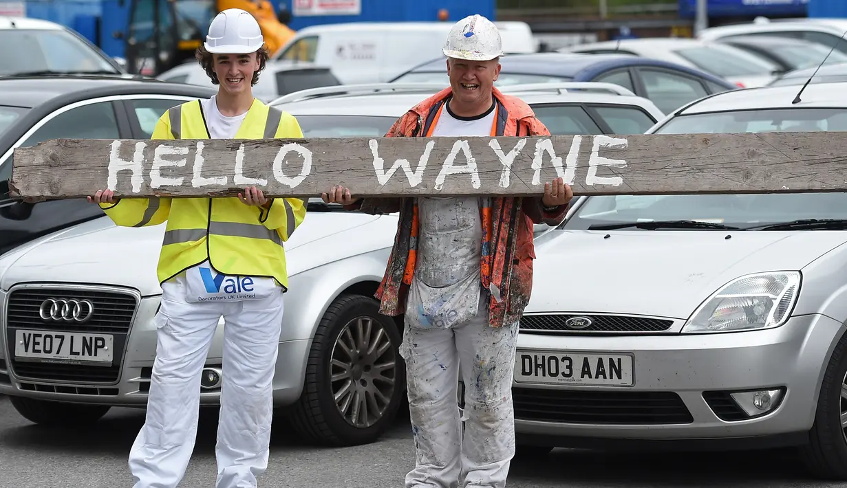 Dua pekerja menyambut pemain baru Everton, Wayne Rooney di luar Goodison Park di Liverpool (10/8). Selama 13 tahun memperkuat Manchester United akhirnya Wayne Rooney kembali klub yang membesarkan namanya Everton. (AFP Photo/Paul Ellis)