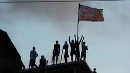 Para tahanan mengibarkan bendera diatas atap usai bentrokan antar dua geng narkoba di penjara Alcacuz, Rio Grande do Norte, Brasil, (16/1). Sebagian besar jenazah ditemukan dalam kondisi termutilasi. (AFP Photo/Andressa Anholette)
