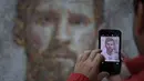 Seorang pengunjung mengambil gambar mural Lionel Messi di Casa Rosada Museum, Buenos Aires, Argentina, Rabu (20/6). Mural terbuat dari dua ribu stiker figur pemain Argentina dalam Piala Dunia sepanjang masa. (Eitan ABRAMOVICH/AFP)
