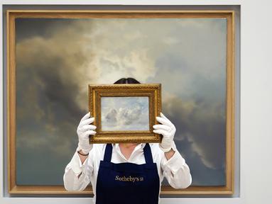 Seorang staf memegang lukisan 'Cloud Study' karya John Constable dengan latar belakang 'Study for Clouds' karya Gerhard Richter di Sotheby's, London, Inggris, 22 Juni 2022. Lukisan yang akan dilelang pada 29 Juni 2022 itu diperkirakan memiliki harga 100.000-150.000 pound, sedangkan 'Study for Clouds' 6-8 juta pound. (AP Photo/Alberto Pezzali)
