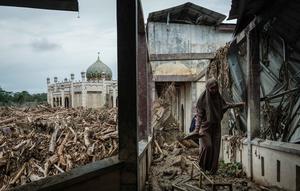 Seorang siswi berjalan di atas bangku untuk menghindari lumpur karena tumpukan pohon tumbang yang tersapu banjir bandang masih berada di Pesantren Darul Mukhlisin dan masjid yang terhubung dengannya di Aceh Tamiang, pada Minggu 14 Desember 2025. Pemandangan memprihatinkan masih terlihat di Pondok Pesantren Darul Mukhlisin, Aceh Tamiang, Minggu (14/12/2025). (Yasuyoshi Chiba/AFP)