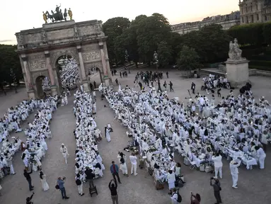 Para peserta dalam balutan serba putih  berkumpul untuk Dinner en Blanc atau "makan malam putih" di Tuileries Gardens, Paris, Kamis (6/6/2019). Gelaran yang berlangsung sejak 1988 ini dilengkapi dengan meja makan yang dihiasi taplak, kursi dan peralatan makan bernuansa putih. (Lucas BARIOULET/AFP)