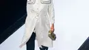 Paula mengenakan trench coat putih dengan monogram khas Vivi Zubedi yang dipadukan dengan celana hitam panjang.  [@vivizubedi].