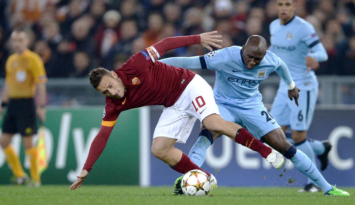 Pemain AS Roma, Francesco Totti (kiri) berebut bola dengan pemain Manchester City, Eliaquim Mangala pada laga Liga Champions 2014/2015 di Olympic Stadium, Roma, 10 Desember  2014. Jersey milik AS Roma pada musim 2014/2015 terlihat polos tanpa sponsor dengan warna merah gelap dan beraksen orenye di lengannya. (AFP/Filippo Monteforte)
