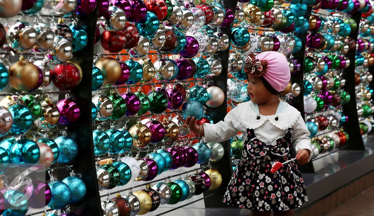 Seorang anak bermain di depan ribuan Bola bertuliskan harapan tergantung di pagar jembatan Eco Skywalk di Mall Central Park, Jakarta, Senin Malam (19/12). (Liputan6.com/Johan Tallo)