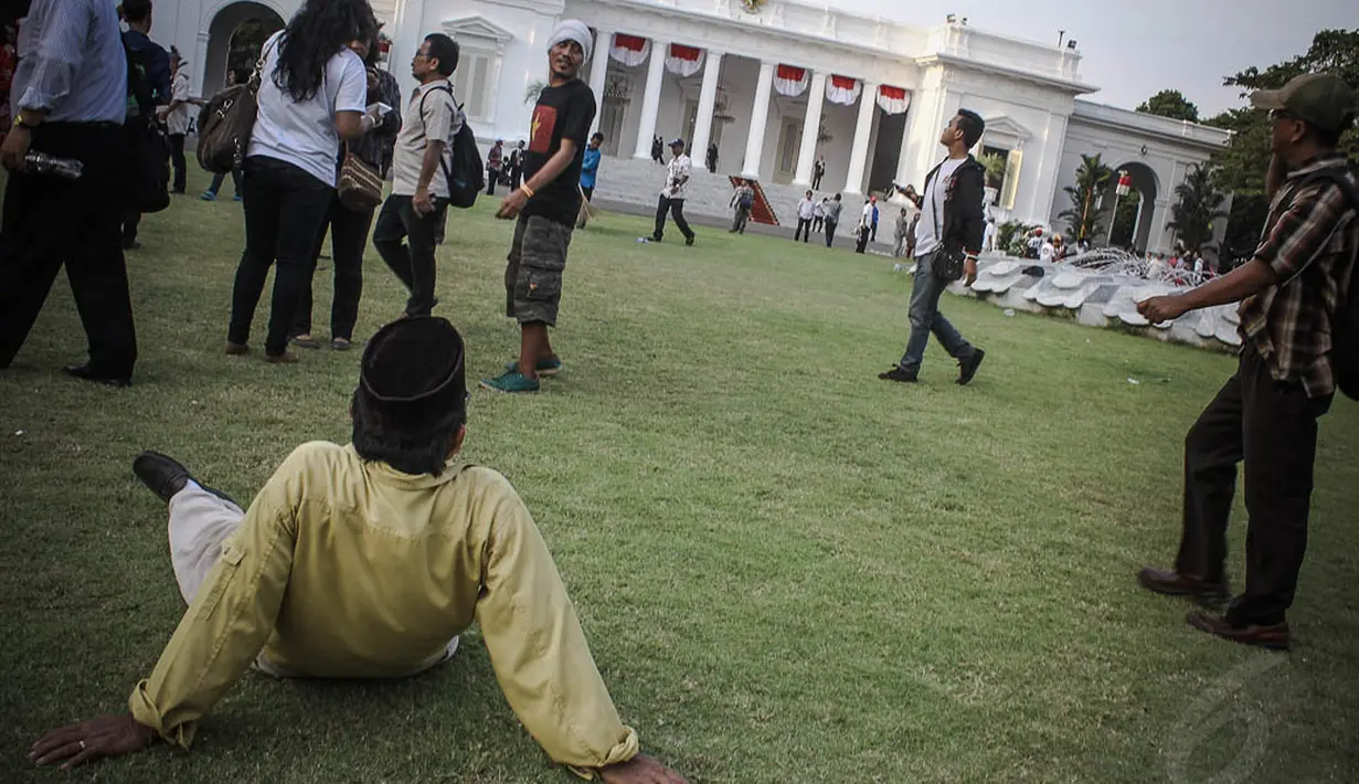 Para warga terlihat ada yang duduk di rerumputan lapangan upacara Istana Merdeka Jakarta, (20/10/14). (Liputan6.com/Faizal Fanani)