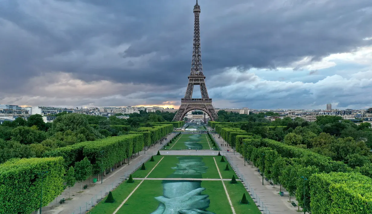 Foto udara dari lukisan raksasa "Beyond Walls" karya seniman jalanan Prancis, Saype, yang terbentang di halaman Champs de Mars, depan Menara Eiffel di Paris, 13 Juni 2019. Karya berukuran 600 meter itu bentuk dukungan kepada organisasi amal penyelamat migran, SOS Mediterranee. (Eric FEFERBERG/AFP)