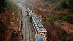 Personel darurat berdiri dekat kereta komuter yang tergelincir dari rel di Vacarisses, Barcelona, Selasa (20/11). Sedikitnya 1 orang tewas akibat longsor yang menerjang sebuah kereta hingga menyebabkannya kereta keluar jalur. (Pau Barrena/AFP)