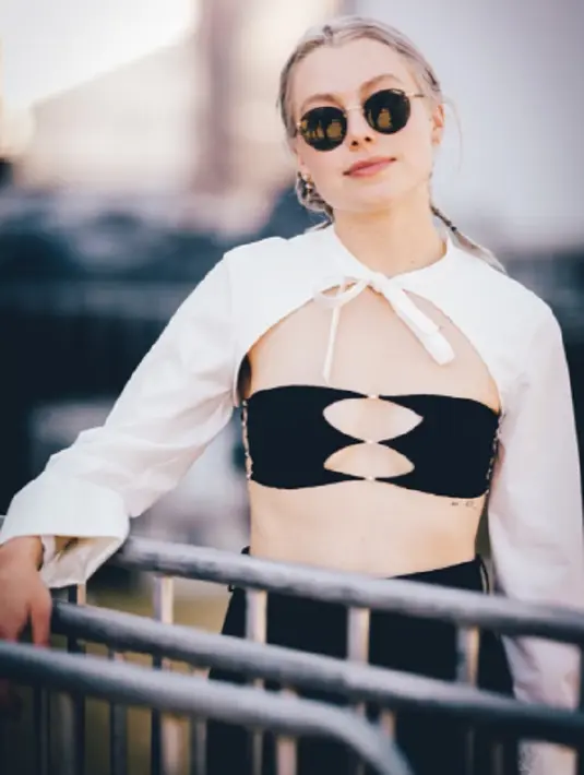 <p>Phoebe Bridgers tampil super edgy dengan black bandeau top, dipadunya dengan shirting-style shrug putih dengan detail pita di bagian leher. Foto: Bustle.</p>