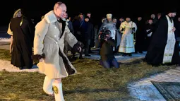 Presiden Rusia Vladimir Putin berpakaian mantel kulit domba berjalan untuk berendam di air dingin selama perayaan Hari Epiphany di Danau Seliger di desa Svetlitsa, Rusia (19/1). (Alexei Druzhinin, Sputnik, Kremlin Pool Photo via AP)