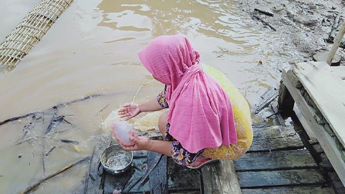 Seorang perempuan menyiangi ikan di pinggir Sungai Batanghari di Desa Manis Mato, Muaro Jambi. (Liputan6.com/Gresi Plasmanto)
