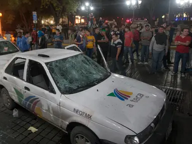 Massa melihat dua mobil milik sebuah stasiun TV yang rusak dalam unjuk rasa kenaikan harga BBM di Monterrey, Meksiko, Kamis (5/1). Unjuk rasa tersebut merupakan protes atas kenaikan harga BBM hingga 20% yang dilakukan pemerintah. (Julio Cesar Aguilar/AFP)