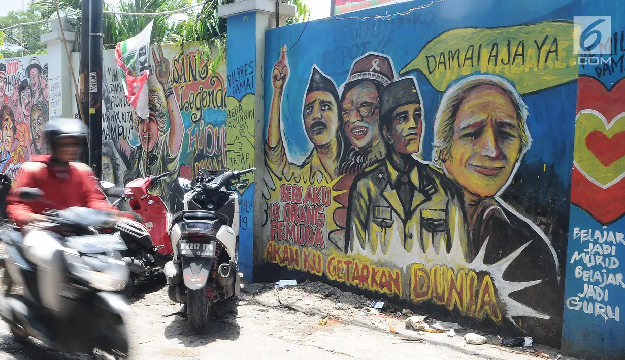 Pengendara motor melintasi mural pemilu di Jalan Karet, Depok, Jawa Barat, Rabu (20/3). Mural tersebut mengajak masyarakat untuk berpartisipasi dalam menyukseskan pemilu dengan cara damai dan menjaga meski berbeda pilihan. (Liputan6.com/Herman Zakharia)
