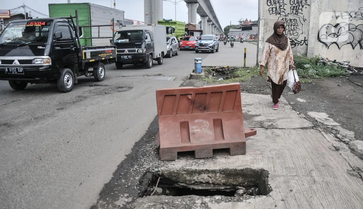 Pejalan kaki melintasi jalan rusak dan berlubang di Jalan Raya Bekasi, Cakung, Jakarta Timur, Selasa (14/3/2023). Minimnya perawatan menyebabkan kondisi Jalan Raya Bekasi arah Cakung ke Pulogebang rusak dan berlubang yang dapat membahayakan keselamatan pengendara, terlebih saat musim penghujan.
