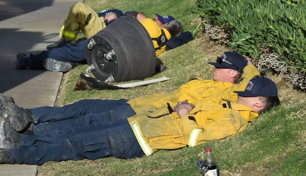 Sejumlah petugas pemadam kebakaran (damkar) beristirahat setelah berusaha menjinakkan kebakaran liar yang disebut Lilac Fire di Bonsall, California, Jumat (8/12). Para petugas damkar itu kewalahan setelah berjuang lebih dari 20 jam. (Robyn Beck/AFP)