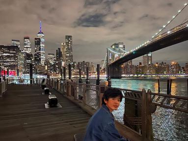Angga Yunanda asyik duduk di pinggir sungai dengan pemandangan jembatan Queensboro Bridge. (Foto: Instagram/@anggayunandareal16)