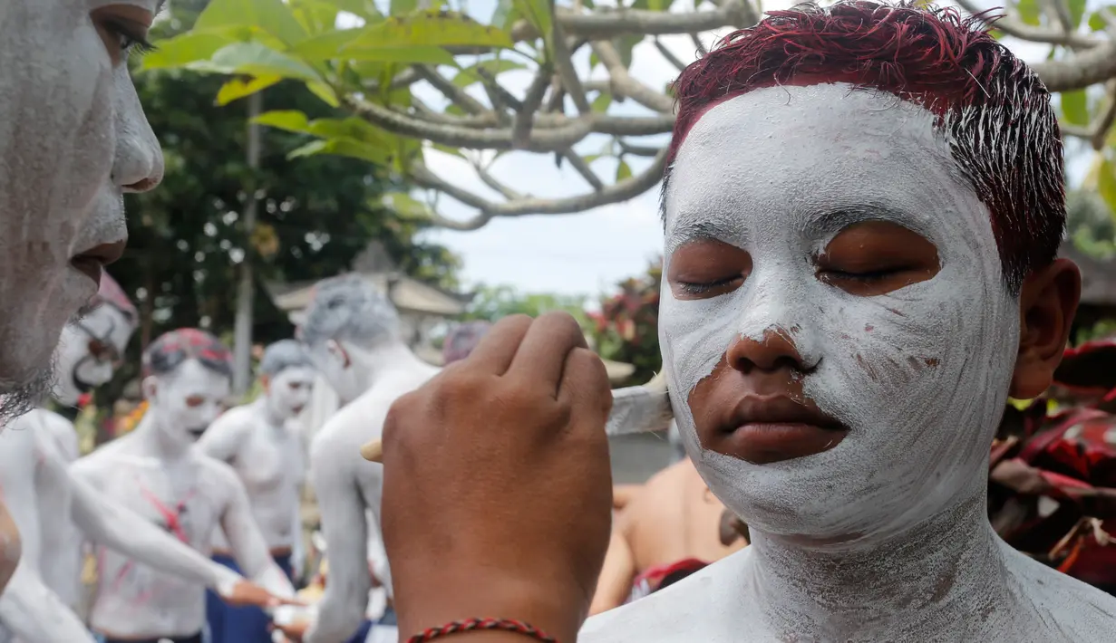 Para pemuda melukis diri mereka untuk persiapan ritual Hindu yang disebut "Grebeg" di Desa Tegallalang, Bali, Rabu (30/1). Tradisi ritual berkeliling kampung dengan riasan tubuh warna-warni itu dipercaya sebagai penangkal Roh jahat. (AP/Firdia Lisnawati)