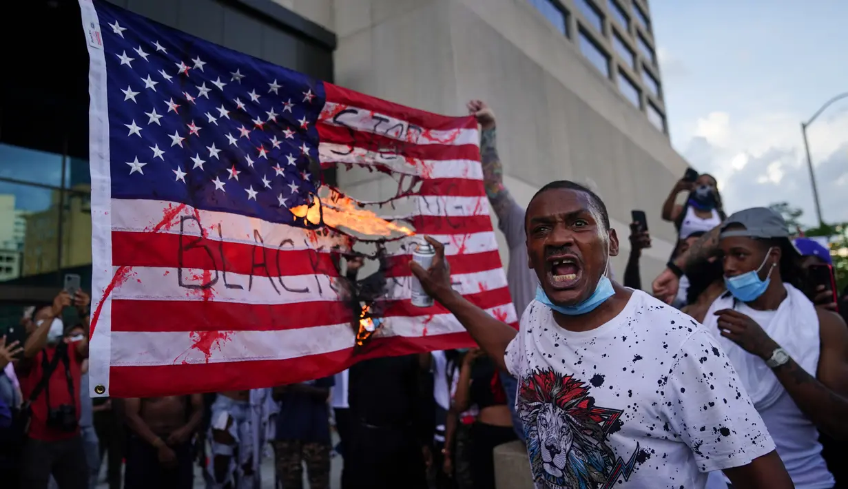 Pengunjuk rasa membakar bendera AS di luar kantor pusat CNN di Atlanta, Georgia, Jumat (29/5/2020). Massa yang mengecam kematian George Floyd (46) oleh polisi melakukan vandalisme dan perusakan gedung CNN pusat. (Elijah Nouvelage/Getty Images/AFP)