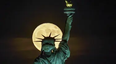 Bulan purnama muncul di depan Patung Liberty, New York, Amerika Serikat, 14 Juni 2022. Fenomena ini disebut juga sebagai Strawberry Supermoon karena terjadi pada saat panen strawberry. (AP Photo/J. David Ake)