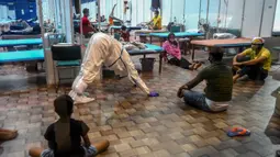 Seorang dokter yang mengenakan setelan Alat Pelindung Diri memberikan instruksi kepada pasien saat melakukan yoga di dalam bangsal di kompleks olahraga Commonwealth Games (CWG) Village yang sementara diubah menjadi pusat perawatan Covid-19 di New Delhi, India, Kamis (16/7/2020). (Money SHARMA / AFP)