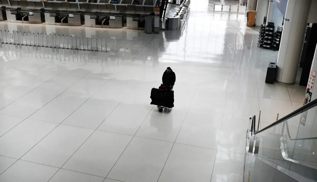 Orang-orang berjalan melalui terminal keberangkatan internasional yang sepi di Bandara John F. Kennedy (JFK), New York City, Sabtu (8/3/2020). Maskapai penerbangan terpukul wabah virus corona (COVID-19) setelah pelancong bisnis maupun rekreasi membatalkan rencana. (Spencer Platt/Getty Images/AFP)