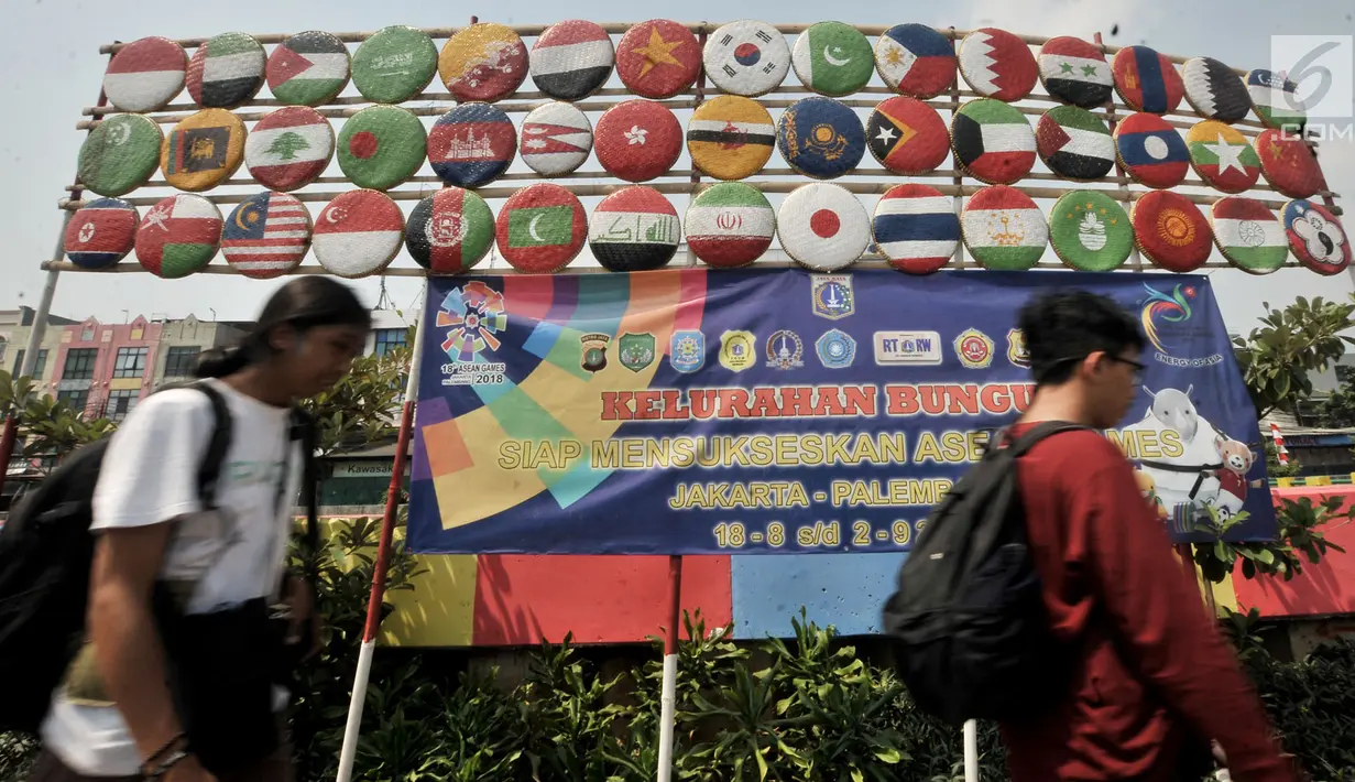 Warga melintas di depan instalasi berupa bendera negara-negara peserta Asian Games 2018, Jakarta, (15/7). Sambut Asian Games, Kelurahan Bungur mempercantik kawasan di pinggir Kali Sunter dengan mengecat warna-warni tembok. (Merdeka.com/Iqbal S. Nugroho)