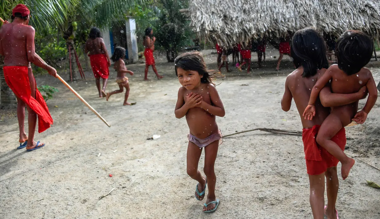 Anak-anak suku Waiapi berjalan di bawah hujan di desa Manilha di negara bagian Amapa, Brasil (14/10). Jumlah anggota suku Waiapi mencapai 1.615 orang, 905 orang diantaranya berada di delapan desa pedalaman Brasil. (AFP Photo/Apu Gomes)