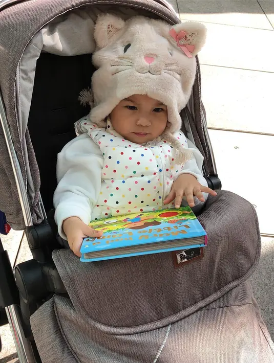 Gadis mungil berusia satu tahun ini memanag takpernah bosan untuk dilihat. Hanya terdiam duduk di strollernya sambil memegang buku  cerita, Natusha tetap saja menarik perhatian publik. (Instagram/natushaa.oliviaa.alinskie)