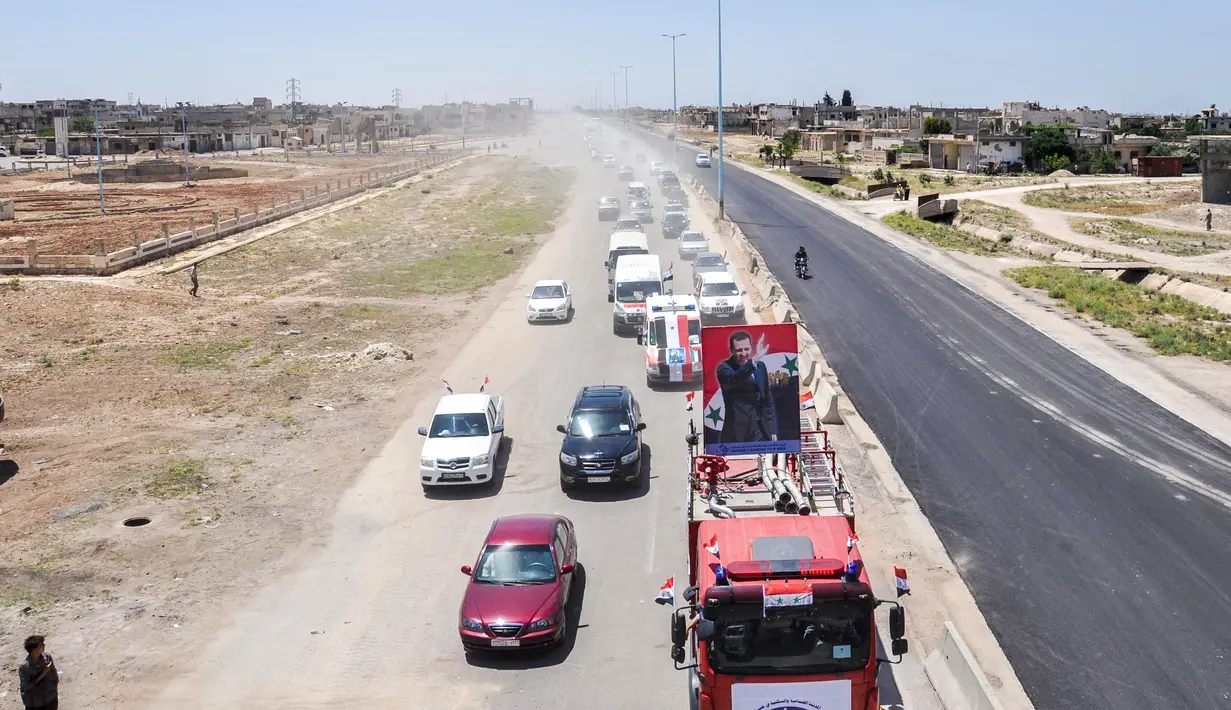 Kendaraan pemerintah dengan bendera nasional Suriah melintasi jalan raya utama antara Homs dan Hama yang dibuka kembali, Rabu (6/6). Pembukaan kembali jalan raya itu menandai kemenangan untuk Presiden Suriah Bashar al-Assad. (AFP/STRINGER)