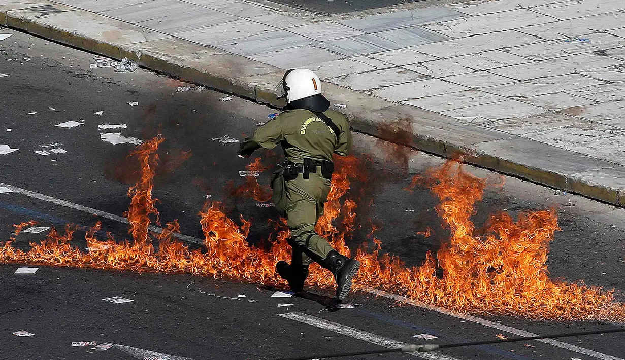Polisi anti huru-hara melwati jalanan yang terbakar api di Athena, Yunani, (12/11/2015). Para Demonstran juga melakukan aksi mogok kerja selama 24 jam. (REUTERS/Yannis Behrakis)