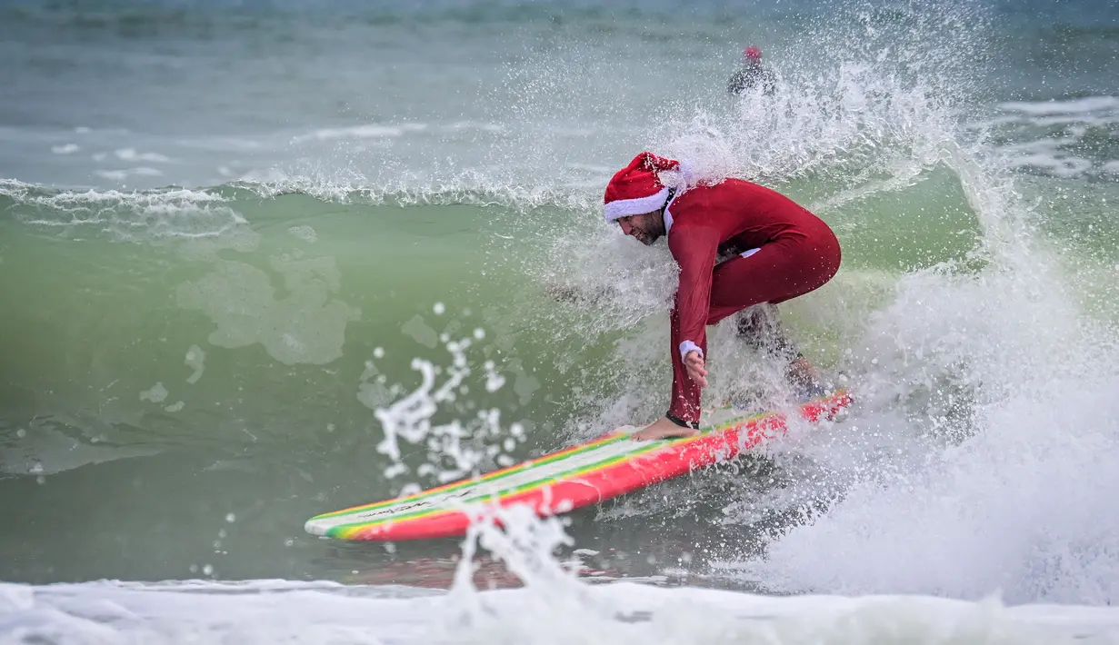 Seorang pengunjung berkostum Sinterklas berselancar dalam acara Surfing Santa yang berlangsung di Pantai Cocoa, Florida, Amerika Serikat, Selasa (24/12/2024) waktu setempat. (AFP/Giorgio Viera)