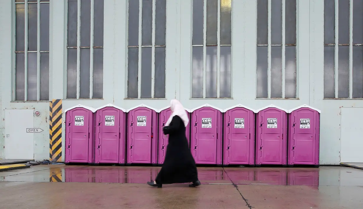 Seorang wanita berjalan melewati deretan toilet portable di tempat penampungan bagi para migran di dalam hanggar bekas bandara Tempelhof di Berlin, Jerman, Rabu (9/12/2015). (REUTERS/Fabrizio Bensch)
