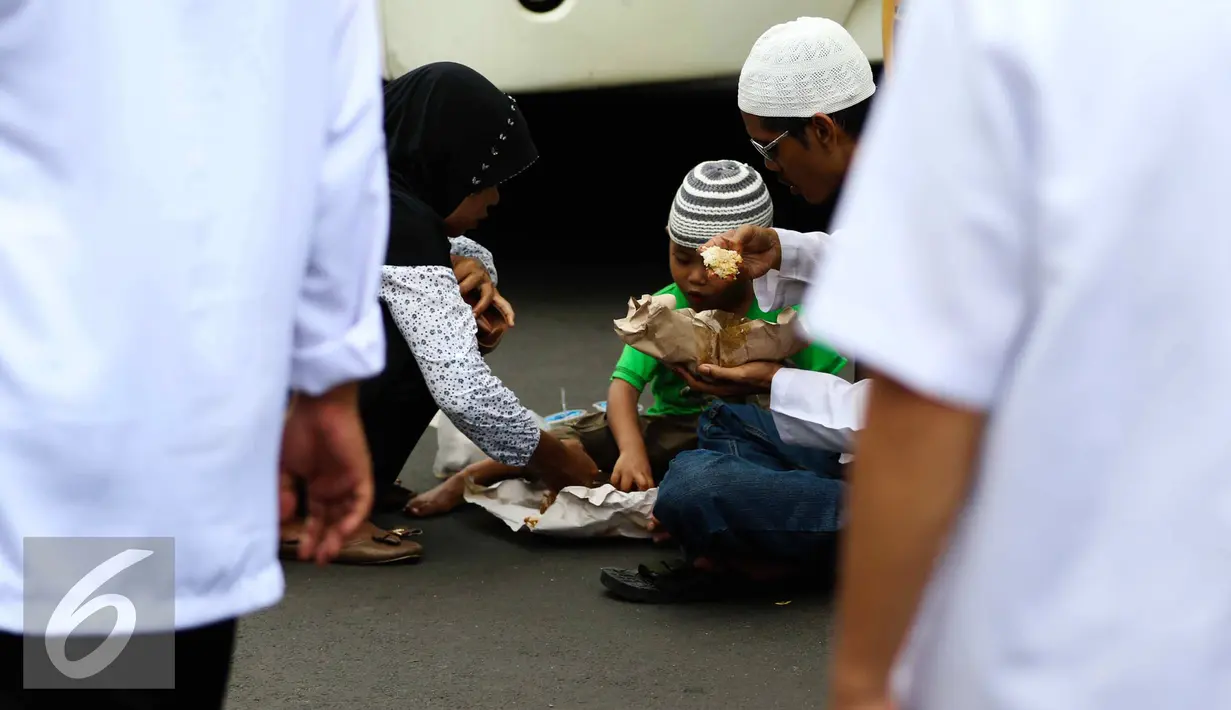 Seorang anak bersama orang tuanya makan siang sebelum memulai aksi di Medan Merdeka Timur, Jakarta, Jumat (4/11). Massa melakukan aksi di depan Istana Negara menuntut penegakan hukum kasus dugaan penistaan agama. (Liputan6.com/Faizal Fanani)