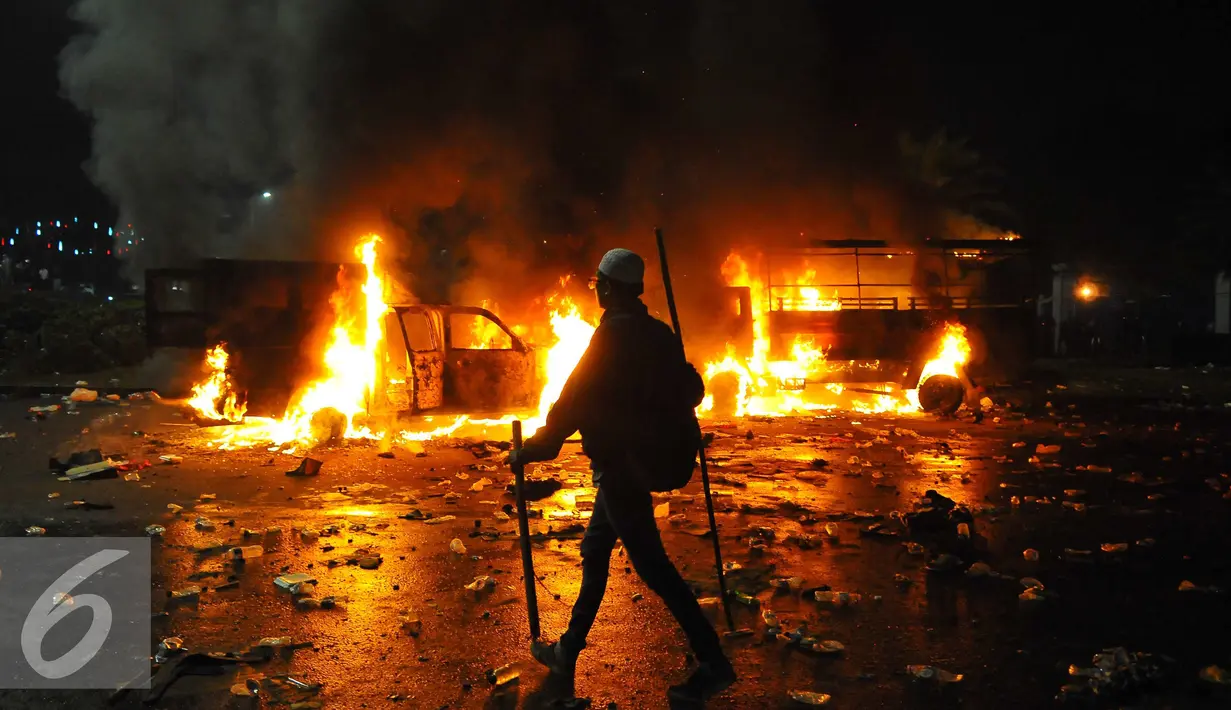 Seorang pendemo melintas di dekat mobil yang terbakar di kawasan Monas, Jakarta, Jumat (4/11). Aksi Damai 4 November ini berakhir ricuh dengan terjadi bentrok antara pendemo versus polisi. (Liputan6.com/Angga Yuniar)