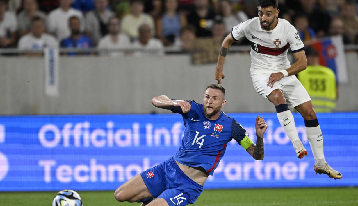 Gelandang Portugal Bruno Fernandes menembak untuk mencetak gol pertama timnya melewati bek  Slovakia Milan Skriniar dalam laga Grup J Kualifikasi Euro 2024 di Stadion Tehelne pole, Bratislava, Sabtu (9/9/2023) dini hari WIB. (AP Photo/Radovan Stoklasa)