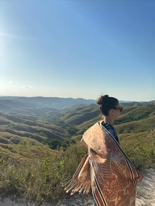 Potret dari belakang menunjukkan Raline Shah yang menyampirkan kain tenun kecokelatan di pundaknya, berlatar pemandangan luar biasa cantik. [Foto: Instagram/ralineshah]