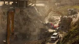 Beberapa buldoser dikerahkan untuk menghancurkan bangunan berisi 13 apartemen di lingkungan Wadi Qaddum, distrik Silwan, selatan Kota Tua Yerusalem. Tampak dalam foto, pasukan Israel berkumpul saat sebuah ekskavator merobohkan sebuah bangunan yang dibangun tanpa izin di lingkungan Wadi Qaddum, Yerusalem timur, pada Senin 22 Desember 2025. (Ahmad GHARABLI/AFP)