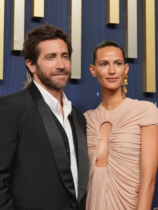 <p>Jake Gyllenhaal mengubah Emmy Awards 2025 menjadi malam kencan langka bersama kekasihnya Jeanne Cadieu. Jake mengenakan tuxedo hitam dengan inner kemeja dan kekasihnya mengenakan gaun berwarna nude dengan belahan di sepanjang dada saat mereka berjalan di karpet merah. Ia mempercantik penampilannya dengan tas genggam emas dan perhiasan emas, serta gaya rambut disisir rapi ke belakang. [AP Photo/Jae C. Hong]</p>