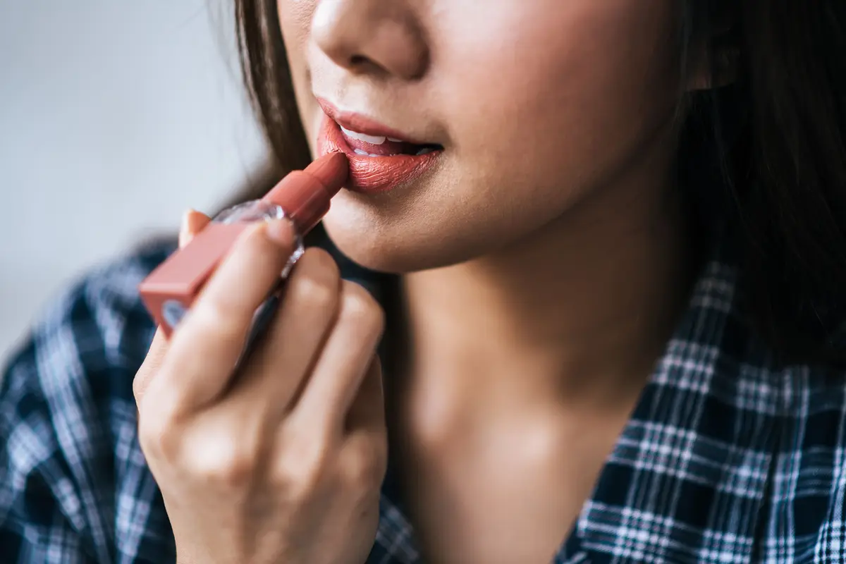 Seorang perempuan sedang mengaplikasikan lipstik di bibirnya (Foto Dok: Freepik/jcomp)