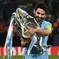 Gelandang Manchester City, Ilkay Gundogan menggendong trofi Liga Champions dalam perayaan kemenangan atas Inter Milan pada laga Final Liga Champions 2022/2023 di Ataturk Olympic Stadium, Istanbul, (10/6/2023). Gelar ini juga menjadi yang pertama bagi sang kapten Man City di laga final kontra Inter Milan. (AFP/Paul Ellis)