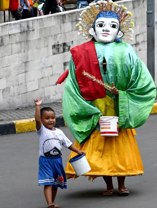 Foto pada 26 April 2019, memeprlihatkan Hassan (4) memegang ember kecil untuk saweran bergabung bersama yang lainnya mengamen ondel-ondel di jalanan Jakarta. Seiring berjalan waktu, ondel-ondel yang dahulu sebagai ikon kesenian Betawi kini mudah ditemui di jalanan ibu kota. (GOH CHAI HIN / AFP)