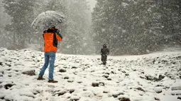 Turis India (kiri) mengambil foto selama hujan salju di Gulmarg, sekitar 55 km sebelah utara Srinagar, Kashmir, Selasa (3/1). Gelombang dingin yang melanda Kashmir kian parah hingga mencapai suhu di bawah nol derajat celcius. (Tauseef Mustafa/AFP)