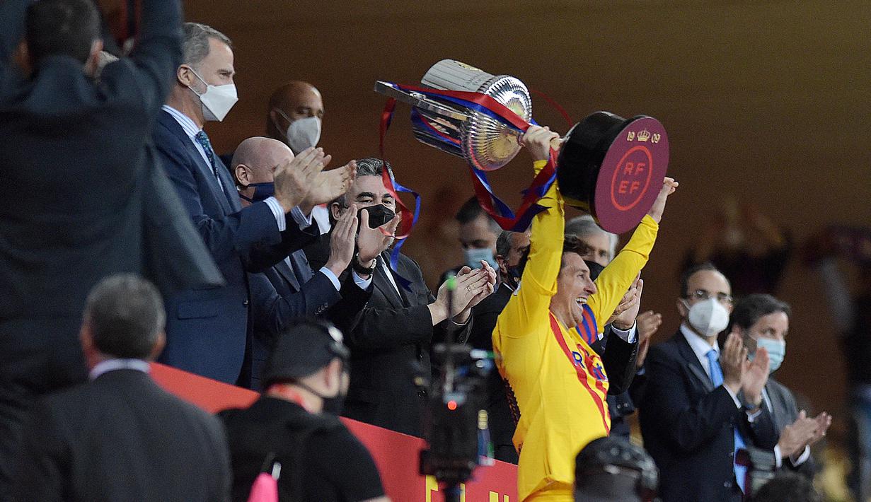 Striker Barcelona, Lionel Messi, mengangkat trofi usai menjuarai Copa del Rey di Stadion Olimpico de Sevilla, Minggu (18/4/2021). Barcelona menang 4-0 atas Athletic Bilbao. (AFP/Cristina Quicler)